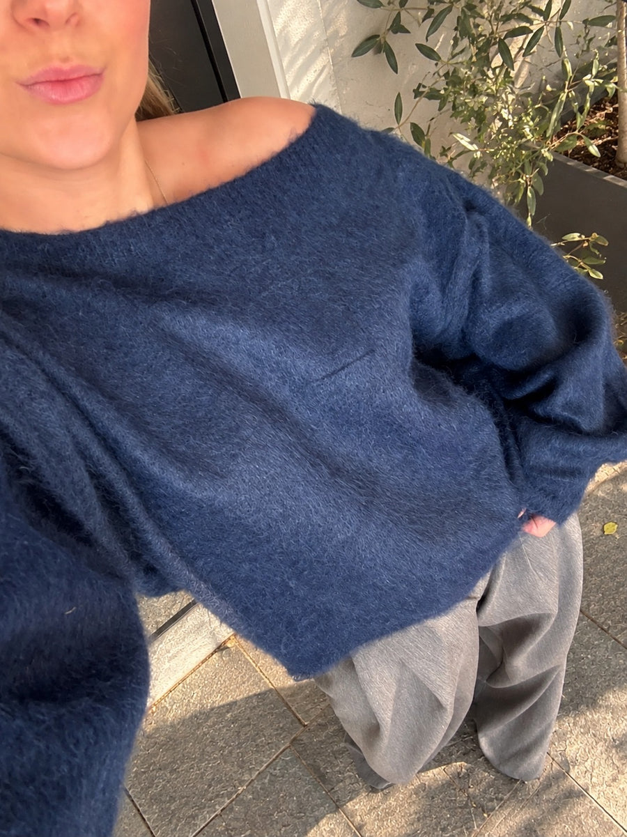 Stijlvolle donkerblauwe off shoulder trui voor dames met een asymmetrische halslijn, korte wijde mouwen en een zachte fluffy structuur. Trendy oversized damestrui in navy blue, een mooie gebreide wintertrui voor herfst en winter 2026 van By Lies.