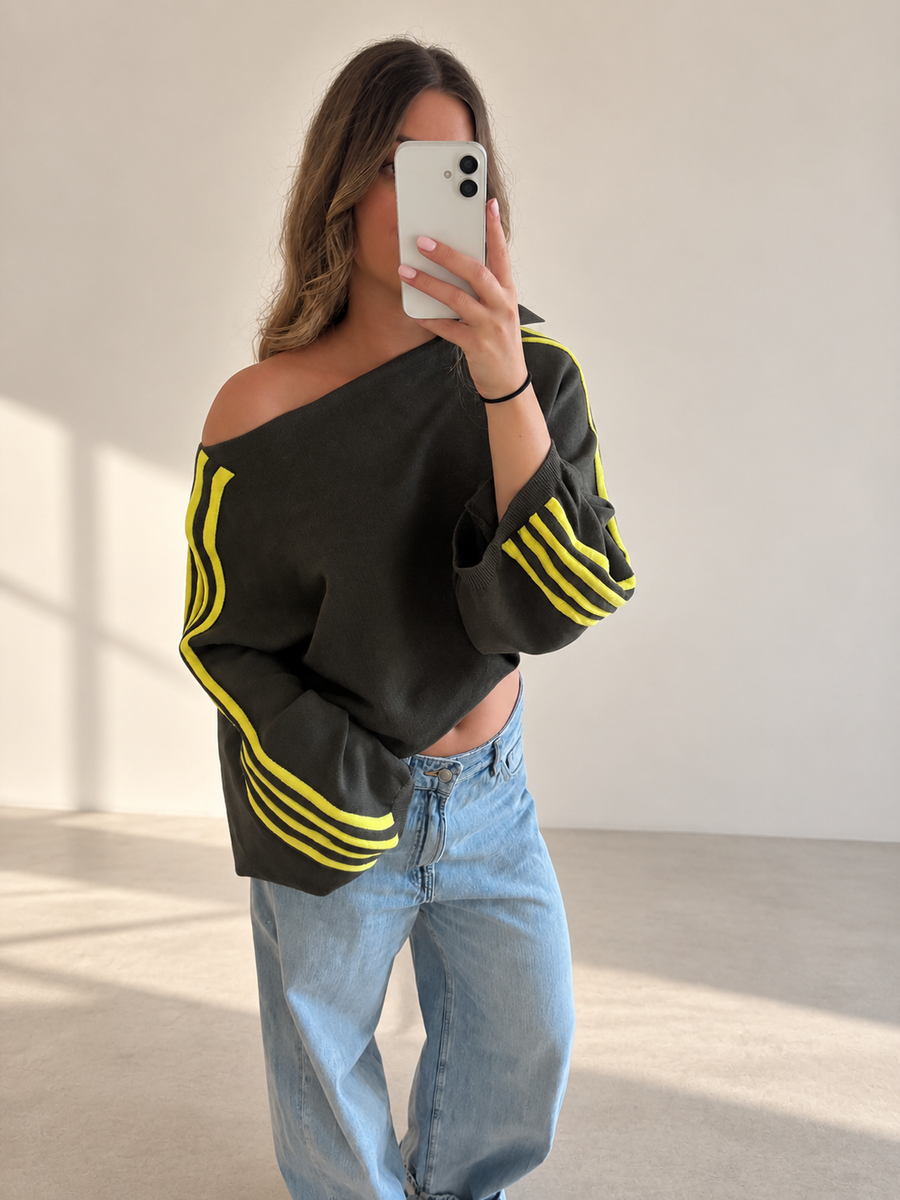 Trendy kaki oversized sweater voor dames met opvallende gele sportstrepen en een off-shoulder pasvorm. Sportieve, comfortabele damessweater met wijde mouwen, een stijlvolle casual look voor herfst en winter 2026. Verkrijgbaar bij By Lies.